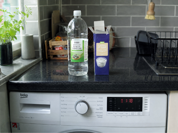 White vinegar and bicarbonate of soda next to a washing machine